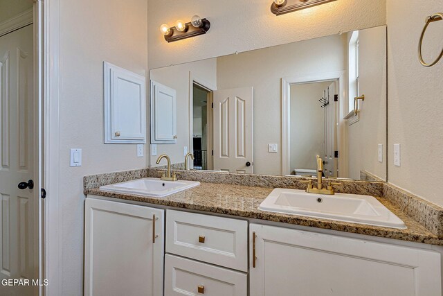 bathroom featuring double vanity, a textured wall, and a sink