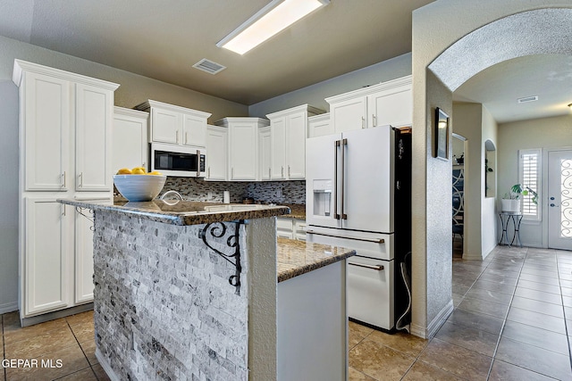 kitchen featuring arched walkways, white refrigerator with ice dispenser, tile patterned floors, white cabinetry, and visible vents