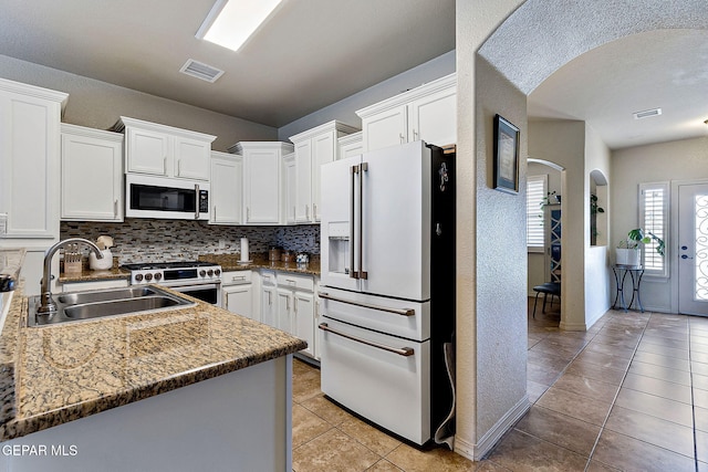kitchen featuring light tile patterned floors, a sink, visible vents, arched walkways, and white appliances