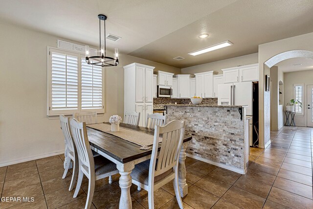 dining space with arched walkways, visible vents, tile patterned floors, and baseboards
