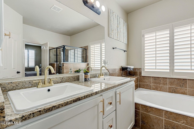 bathroom featuring a bath, a stall shower, double vanity, and a sink