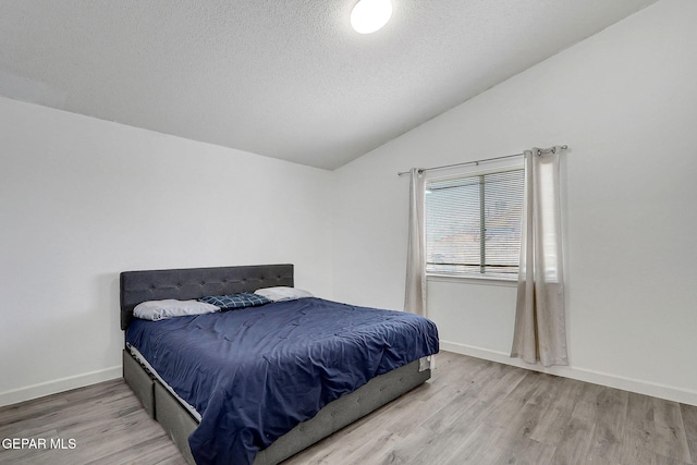 bedroom with a textured ceiling, baseboards, vaulted ceiling, and wood finished floors