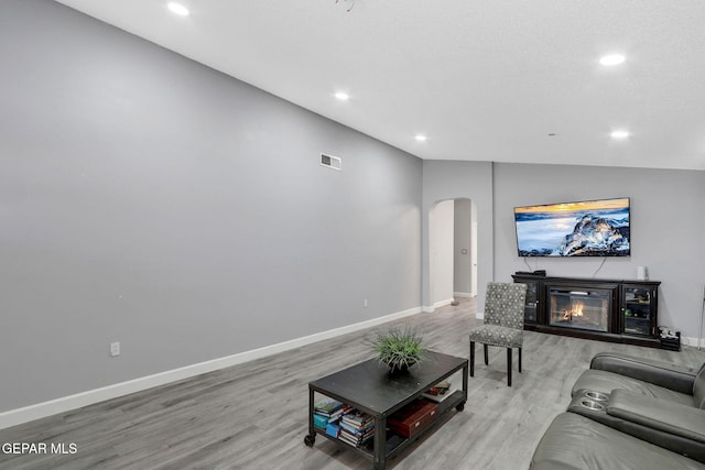 living area featuring arched walkways, recessed lighting, light wood-style flooring, and lofted ceiling