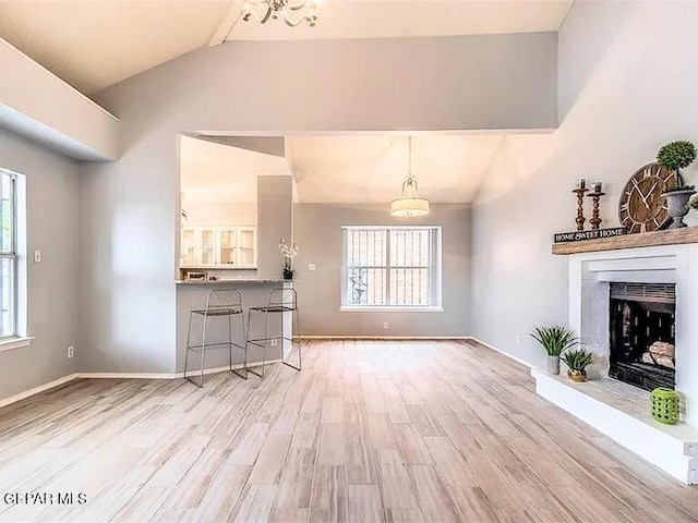 unfurnished living room with a fireplace with raised hearth, baseboards, vaulted ceiling, and wood finished floors