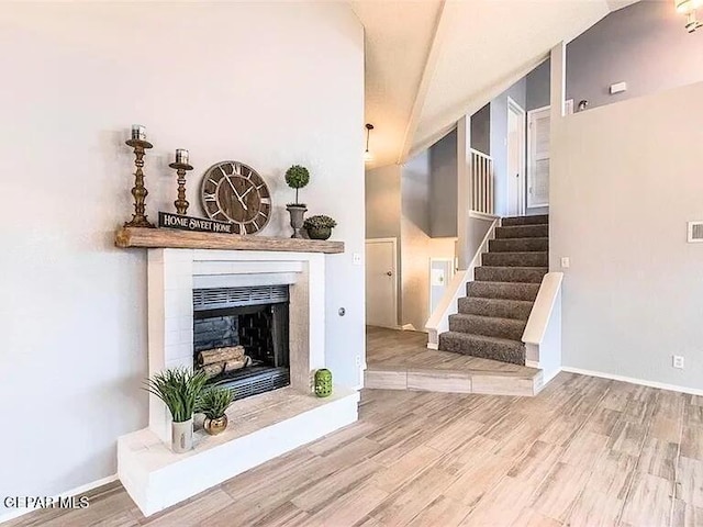 living room with a fireplace with raised hearth, stairs, baseboards, wood finished floors, and lofted ceiling