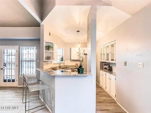 kitchen with a peninsula, a kitchen bar, white cabinets, light stone counters, and a sink