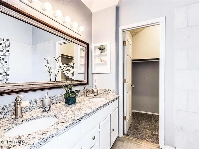 bathroom with a sink, a walk in closet, double vanity, and wood finished floors