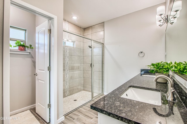 bathroom with a sink, double vanity, baseboards, a shower stall, and wood finished floors