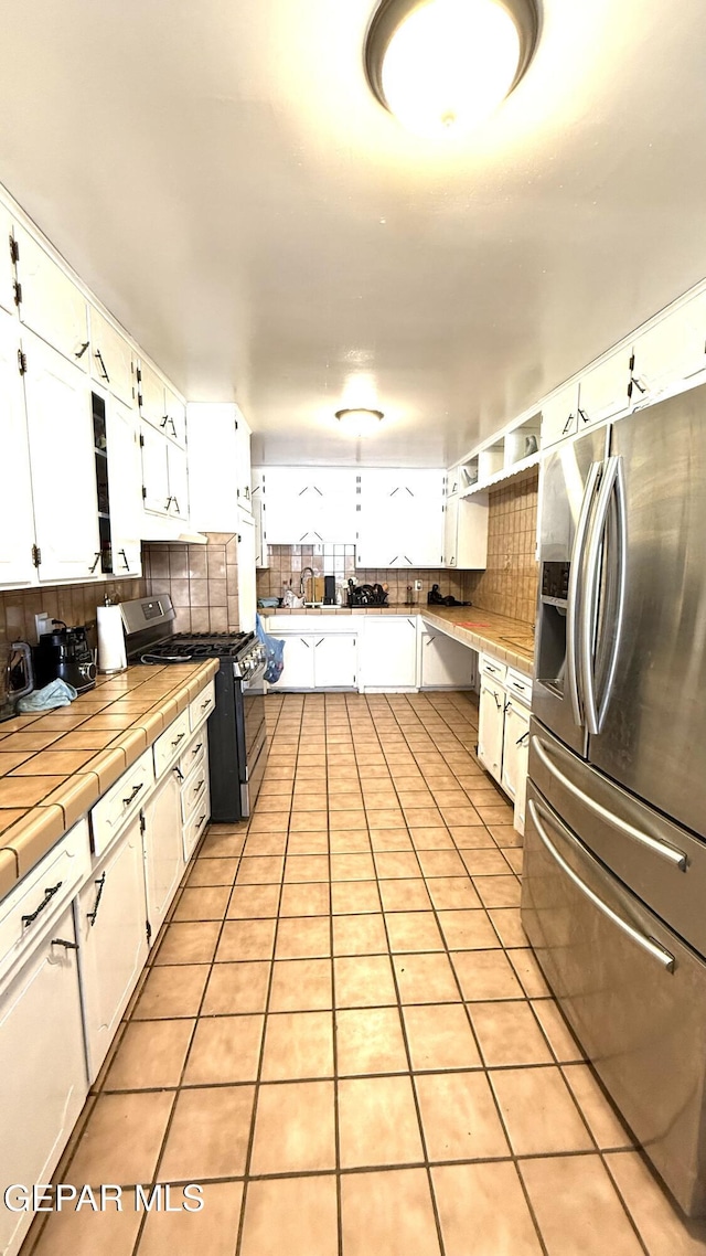 kitchen featuring decorative backsplash, white cabinets, a sink, appliances with stainless steel finishes, and tile countertops