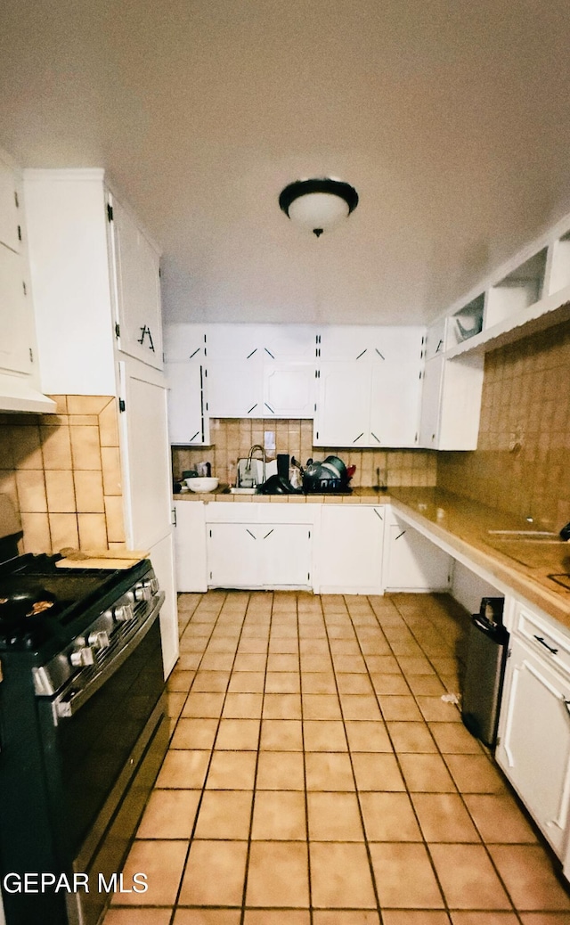 kitchen with tasteful backsplash, stainless steel gas stove, white cabinetry, and a sink