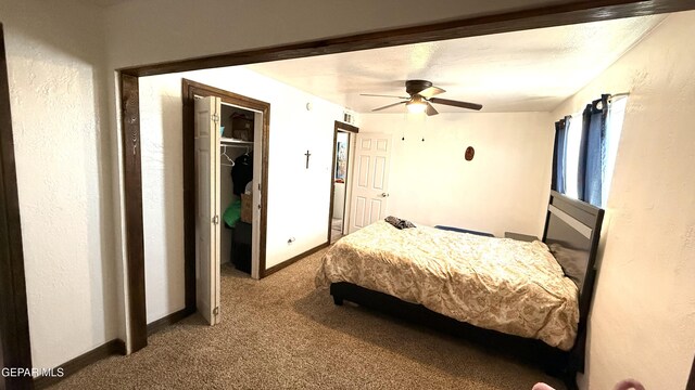 carpeted bedroom featuring a closet, a walk in closet, a ceiling fan, and baseboards