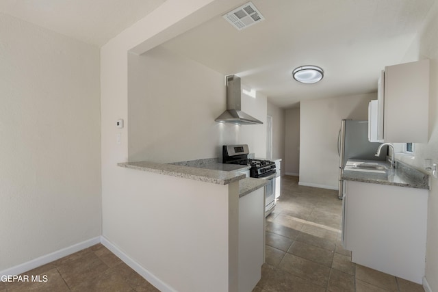 kitchen with a sink, wall chimney exhaust hood, visible vents, gas stove, and white cabinets
