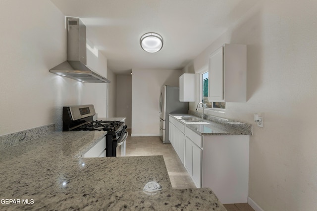 kitchen featuring light stone counters, stainless steel appliances, white cabinets, a sink, and wall chimney exhaust hood