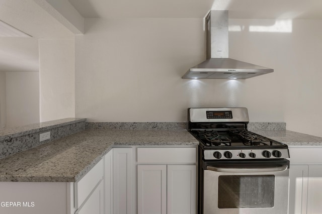 kitchen featuring stainless steel gas range, light stone counters, wall chimney range hood, and white cabinets