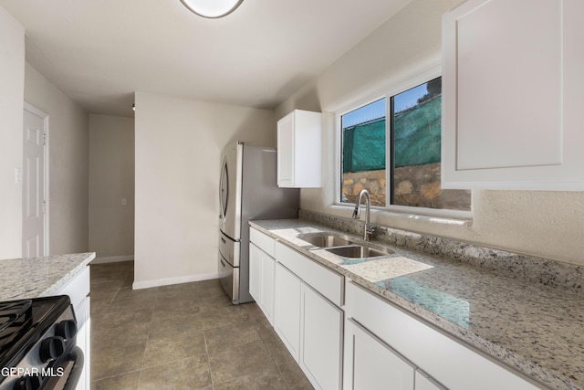kitchen featuring light stone counters, white cabinetry, a sink, stainless steel appliances, and baseboards