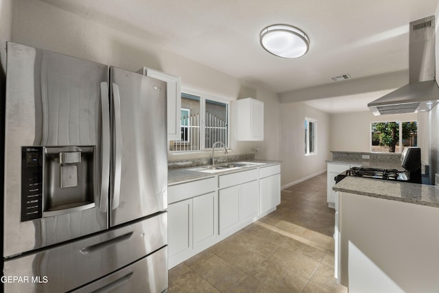 kitchen with a sink, wall chimney range hood, white cabinets, gas range, and stainless steel fridge with ice dispenser