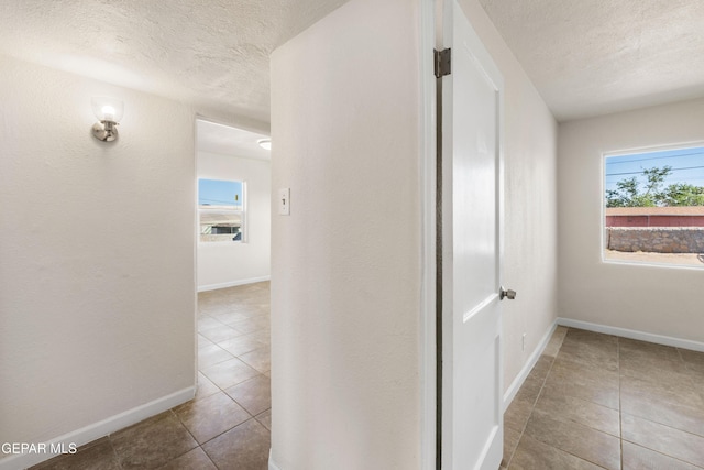 corridor with tile patterned flooring, a textured ceiling, and baseboards