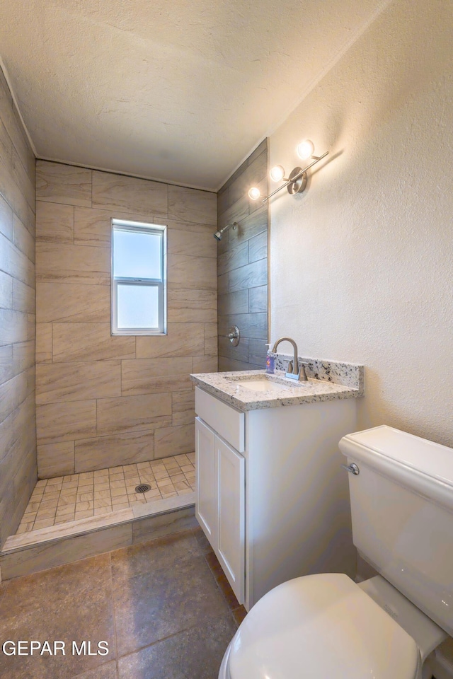bathroom with a tile shower, toilet, and vanity