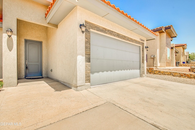 doorway to property with a garage, driveway, a tile roof, and stucco siding