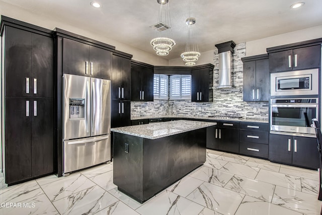 kitchen featuring wall chimney range hood, decorative light fixtures, a center island, a chandelier, and stainless steel appliances