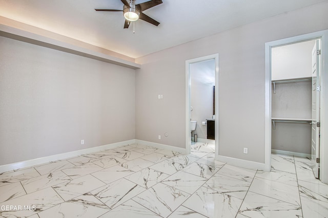 unfurnished bedroom with a closet, marble finish floor, baseboards, ensuite bathroom, and a spacious closet