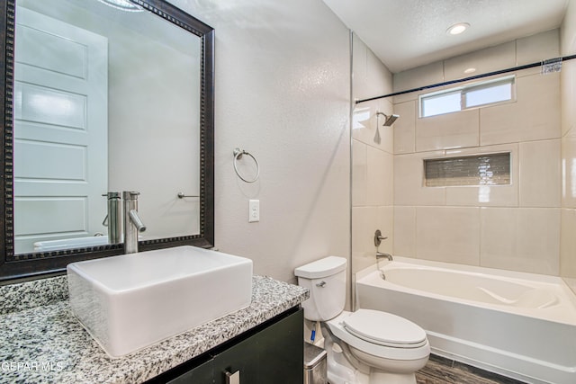 full bath featuring vanity, a textured wall, wood finished floors, toilet, and  shower combination