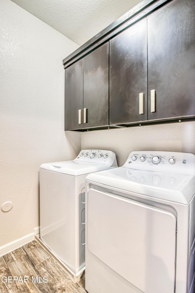 laundry room featuring washing machine and dryer, baseboards, wood finish floors, a textured ceiling, and cabinet space