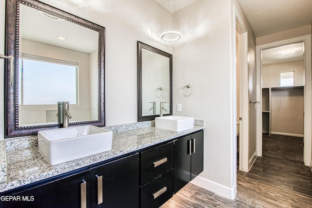 full bathroom with a sink, baseboards, double vanity, and wood finished floors