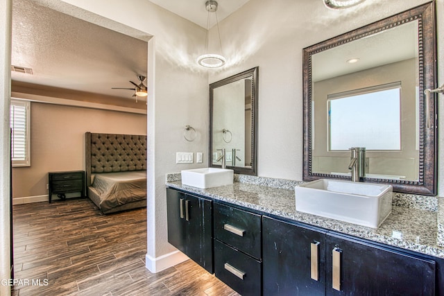 ensuite bathroom with a sink, baseboards, a ceiling fan, and wood finished floors