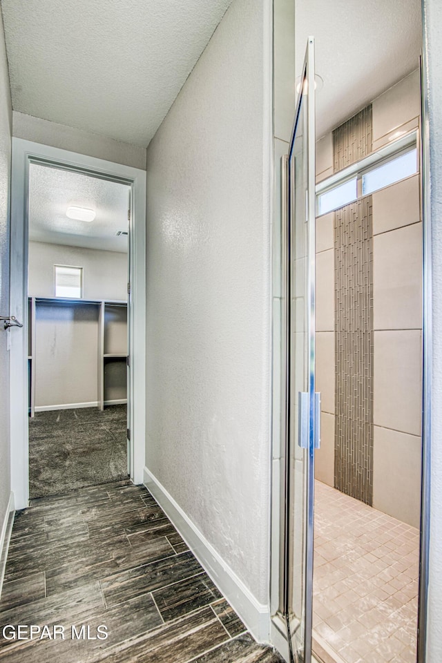hall featuring a textured ceiling, a textured wall, baseboards, and wood finished floors