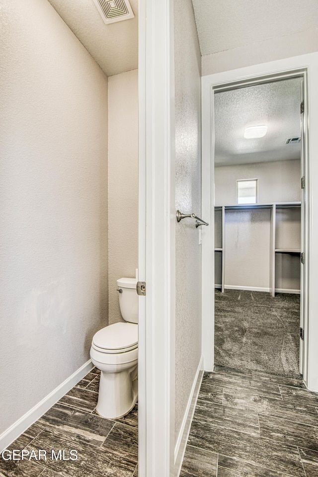 bathroom featuring toilet, a textured ceiling, baseboards, wood finished floors, and visible vents