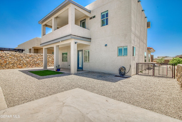 rear view of property with fence, stucco siding, a gate, a patio area, and a balcony