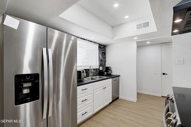 kitchen with visible vents, appliances with stainless steel finishes, dark countertops, a sink, and light wood-style floors