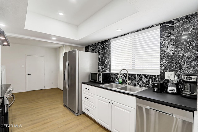 kitchen with dark countertops, appliances with stainless steel finishes, a sink, light wood-style floors, and white cabinetry