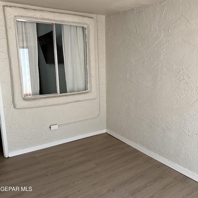 unfurnished room with baseboards and dark wood-type flooring