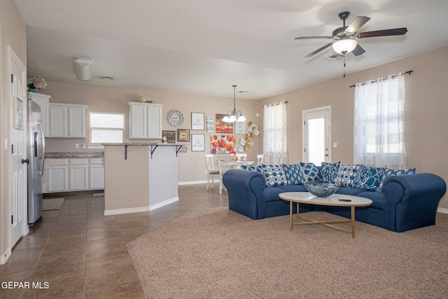 living room with tile patterned floors, visible vents, baseboards, and ceiling fan with notable chandelier