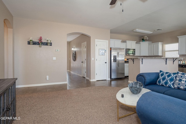 living area featuring baseboards, arched walkways, ceiling fan, and dark tile patterned floors
