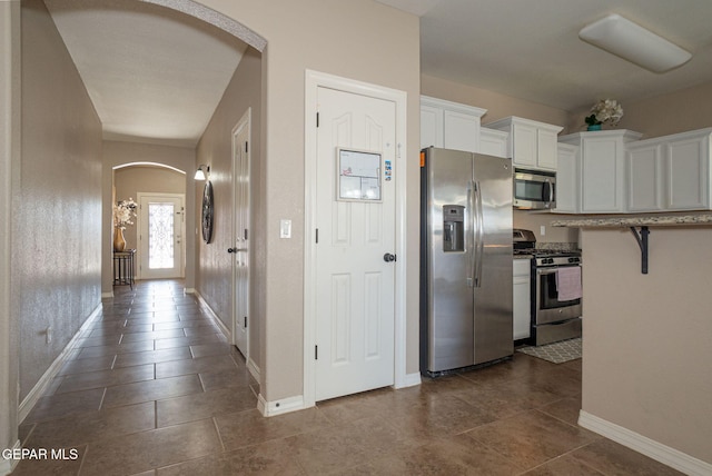 kitchen featuring baseboards, arched walkways, white cabinetry, and appliances with stainless steel finishes