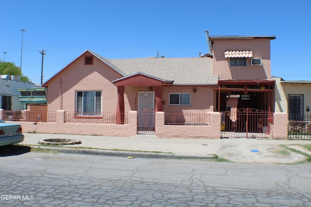 bungalow with a fenced front yard, stucco siding, and roof with shingles