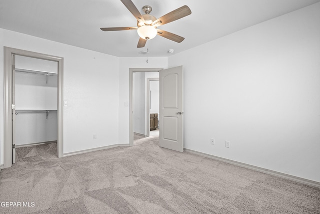 unfurnished bedroom featuring baseboards, carpet flooring, a walk in closet, and a ceiling fan