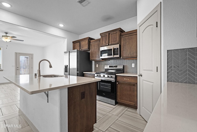kitchen featuring a kitchen island with sink, visible vents, tasteful backsplash, a sink, and stainless steel appliances