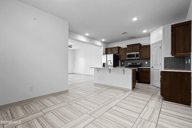 kitchen with decorative backsplash, a breakfast bar area, appliances with stainless steel finishes, a center island with sink, and light countertops