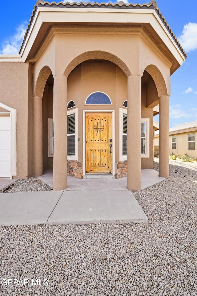 doorway to property featuring stucco siding, a porch, and a tile roof