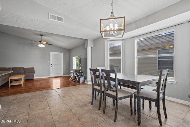 tiled dining room featuring a textured ceiling, visible vents, vaulted ceiling, baseboards, and ceiling fan with notable chandelier