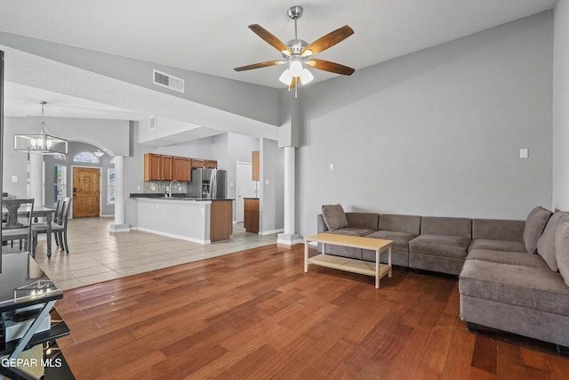 living room featuring arched walkways, ceiling fan with notable chandelier, light wood finished floors, and visible vents