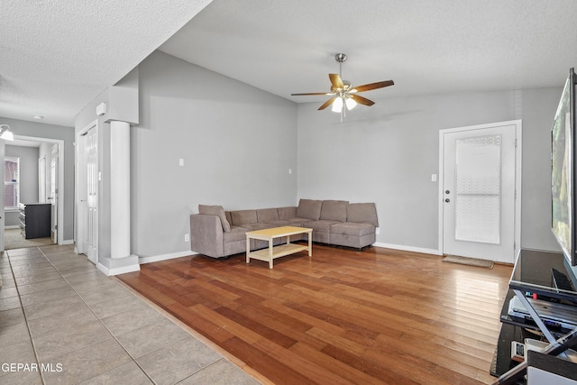 living room with baseboards, a ceiling fan, a textured ceiling, and light wood-type flooring