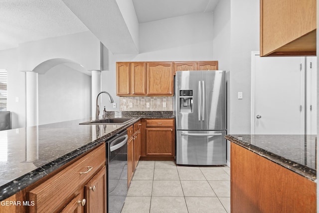 kitchen with a sink, backsplash, stainless steel appliances, and dark stone countertops