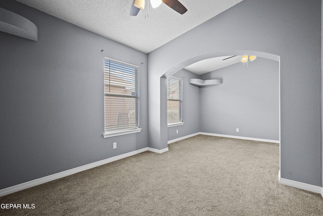 carpeted spare room featuring arched walkways, ceiling fan, baseboards, and a textured ceiling