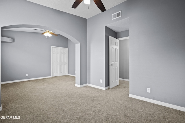 empty room with arched walkways, a ceiling fan, carpet flooring, and visible vents