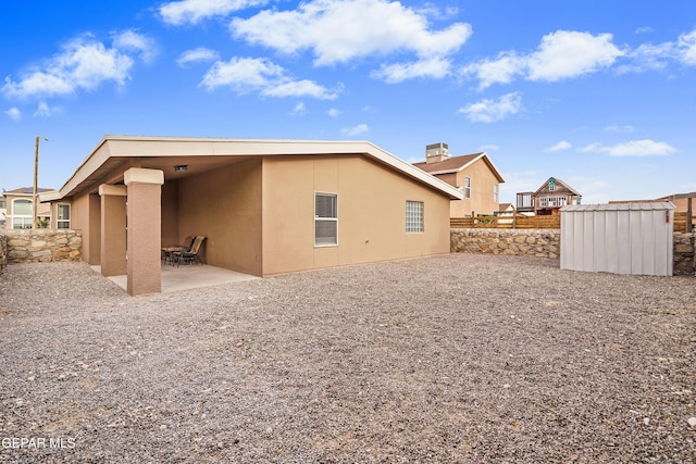back of house featuring an outdoor structure, a patio area, stucco siding, and a storage shed